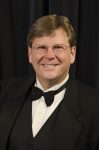 A picture of Dr. Bruce Southard smiling wearing a black suit jacket, a black vest, a white dress shirt and black bow tie.